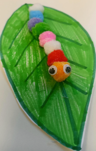 a caterpillar made of tiny pom poms and googly eyes on a paper leaf