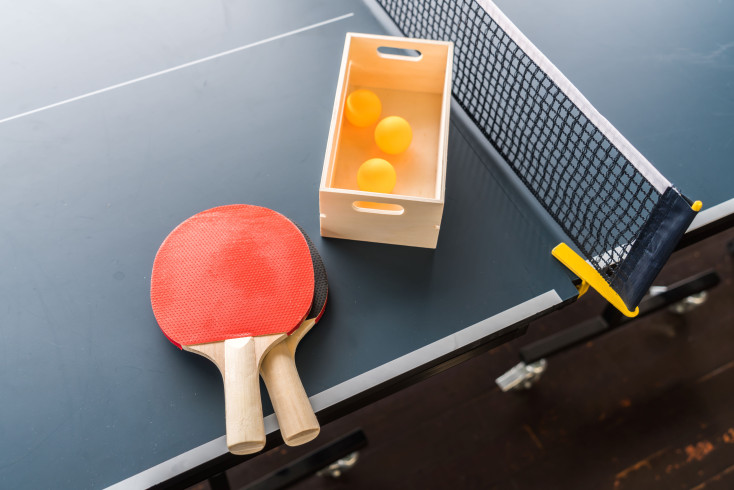 2 red table tennis bats next to a box of orange balls are placed ontop of a table tennis table