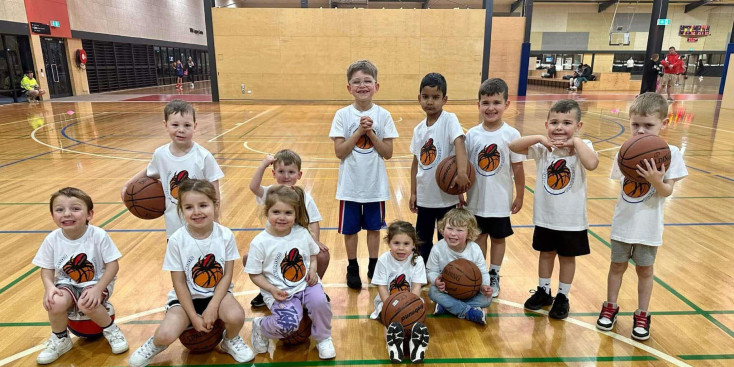a group of kid in white t shirts with a basketball on are smiling at the camera