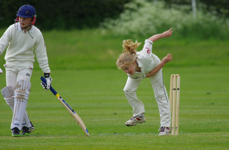 a girls has just bowled a cricket ball and a boy is getting ready to run