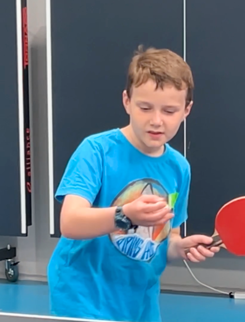 a boy in a blue t shirt is getting ready to hit a table tennis ball with a red bat