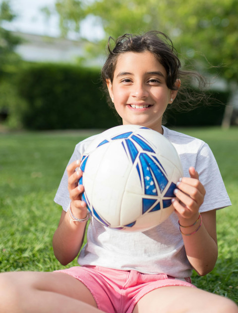 a girl in a white t shirt is holding a Football and smiling at the camera