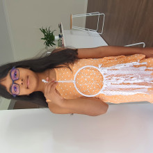 Myra, in an orange dress, poses with her dream catcher made of white fabric and lace
