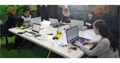 Young people sit around a desk each looking at their own laptop