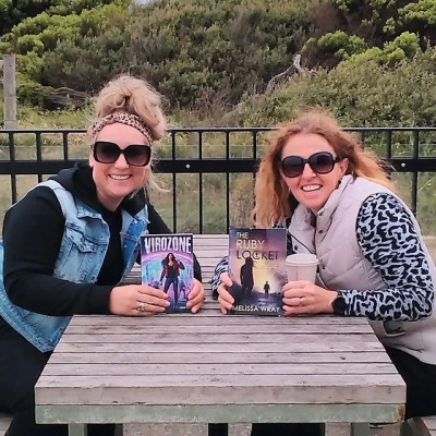 Two authors hold copies of their books on a table outside