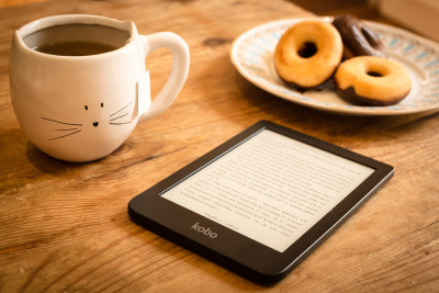 an ebook reader with a full mug and plate of pastries