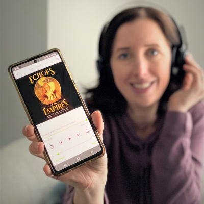 Librarian Katy Anne holds a phone with Echoes and Empires audiobook playing