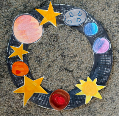 a wreath made as per instructions in Space Wreath. It's got colourful stars and planets on the rim of a painted paper plate.