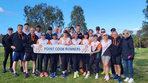 a group of people stand and smile at the camera holding a banner which says Point Cook Runners