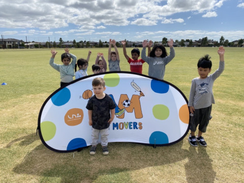 Little kids are standing around a Mini Movers sign holding up their hands