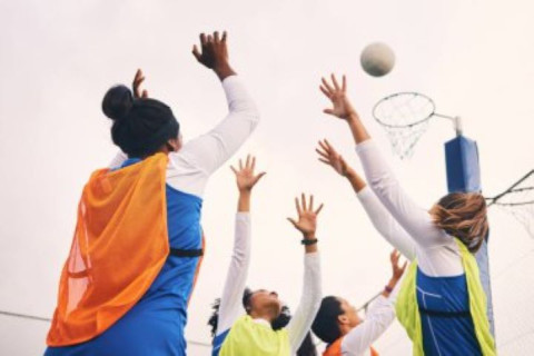 a group of girls wearing netball bibs are reaching up to a netball in the air