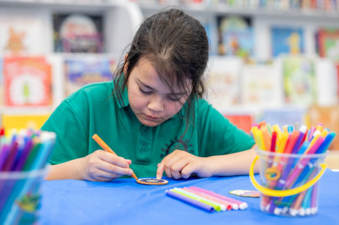 A girl colours in a wooden craft with bright textas.