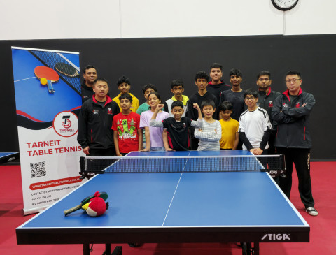 children and adults are standing behind a table tennis table and smiling at the camera