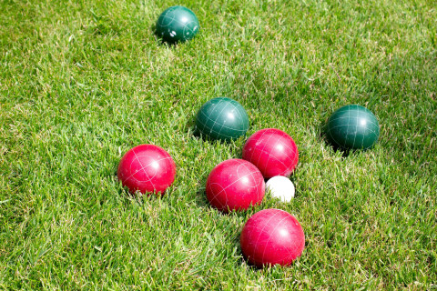 red and green lawn bowls are clustered around a white jack ball