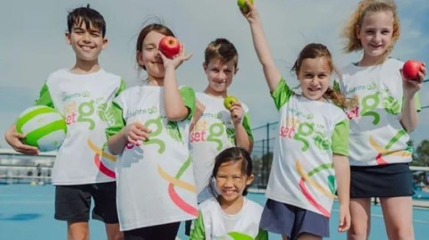 a group of kids in white and green NetSetGo T shirts are cheering at the camera
