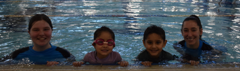 2 adults and 2 kids are in a pool smiling at the camera