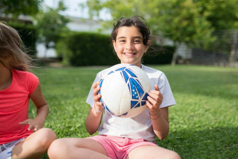 a girl in a white t shirt is holding a Football and smiling at the camera