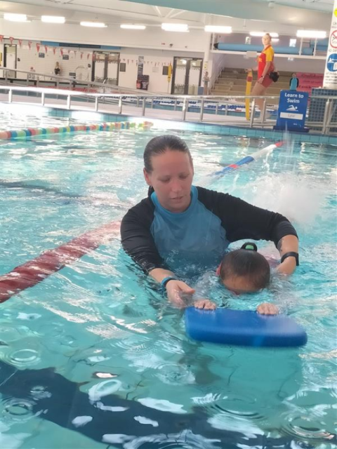 A swimming instructor is helping a child to swim with a float in the pool