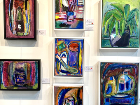 Close-up photo of 6 colourful paintings by local artist James Lazaridis, displayed on a wall.