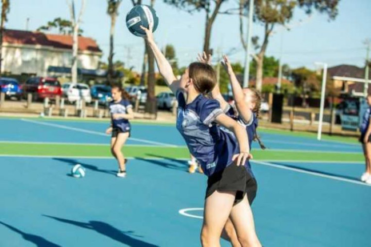 a girl reaches out to catch a ball, outside on a Netball court