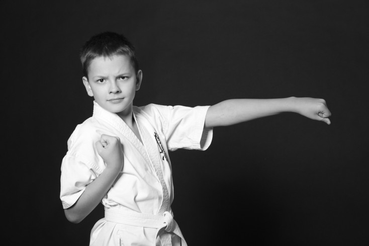 a boy in a karate outfit is standing with one hand straight to look like a punch