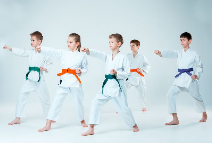 group of boys and girls in karate uniforms standing with one arm forwards in a punching stance