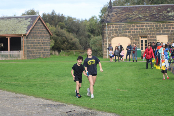 two children are running together, they are both holding a guiding strap