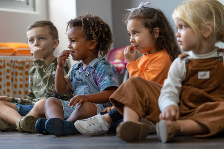 Four young children sit on the floor and practise Auslan signs.