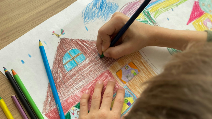 Child drawing a house with pencils