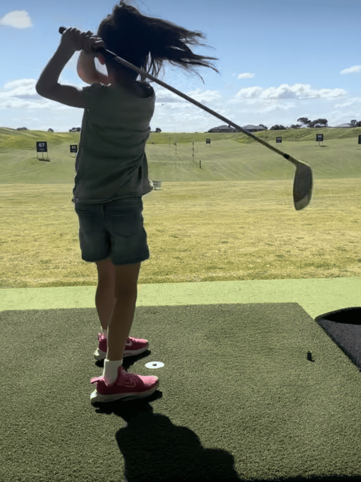 a girl wearing shorts and t shirt has just hit a golf ball into the distance with a golf club