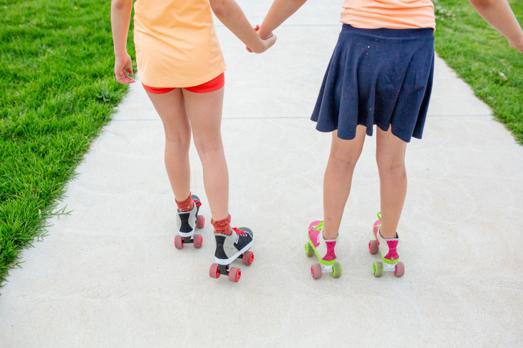 two girls holding hands are roller skating away from the camera
