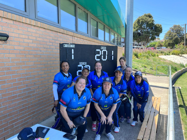 a group of women in blue team cricket uniforms are gathered infront of a scoreboard