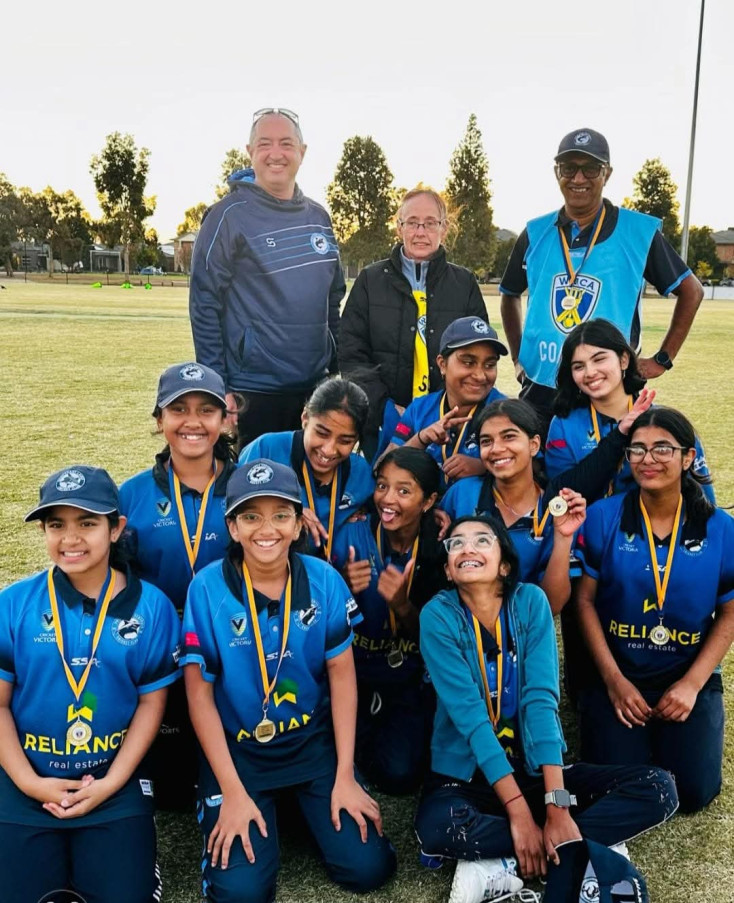 a group of girls in cricket kit are smiling at the camera