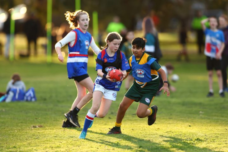 a girl is running with a Footy ball and a boy is chasing her