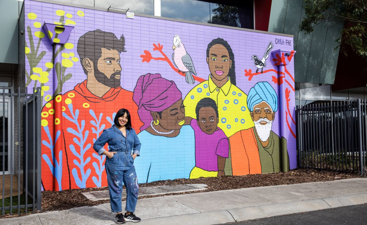 Image: Camila Paz with her commissioned mural “Whispers of the Land, Threads of Belonging” at Penrose Community Centre. Credit: Jack Gruber.