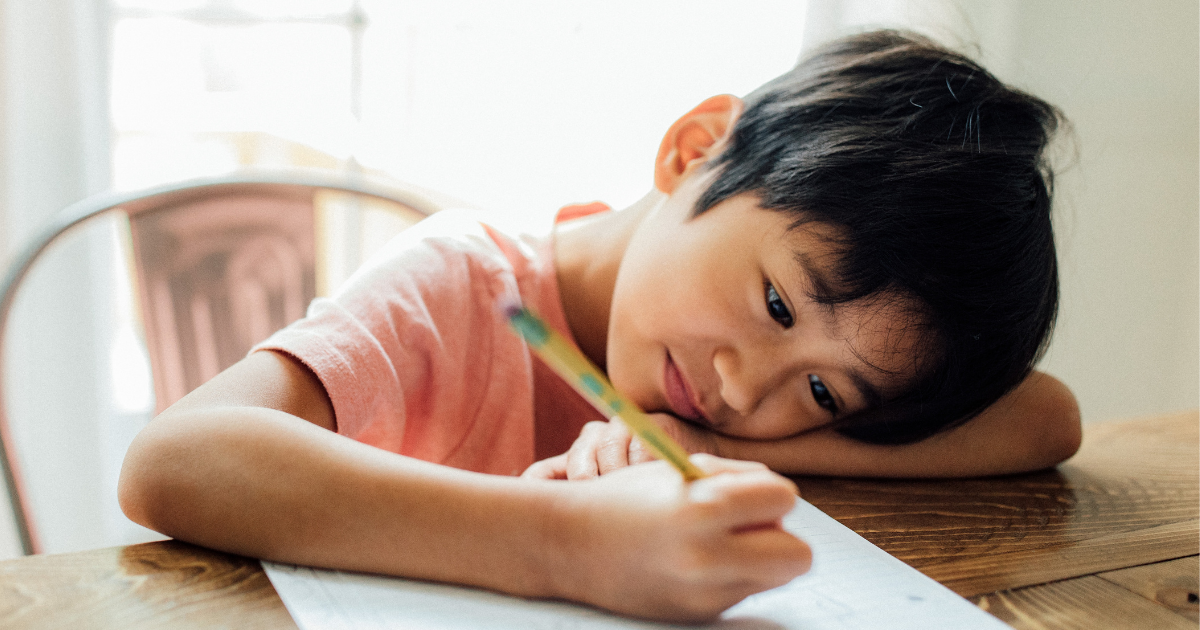 a child leans over a paper with a pencil ready to write