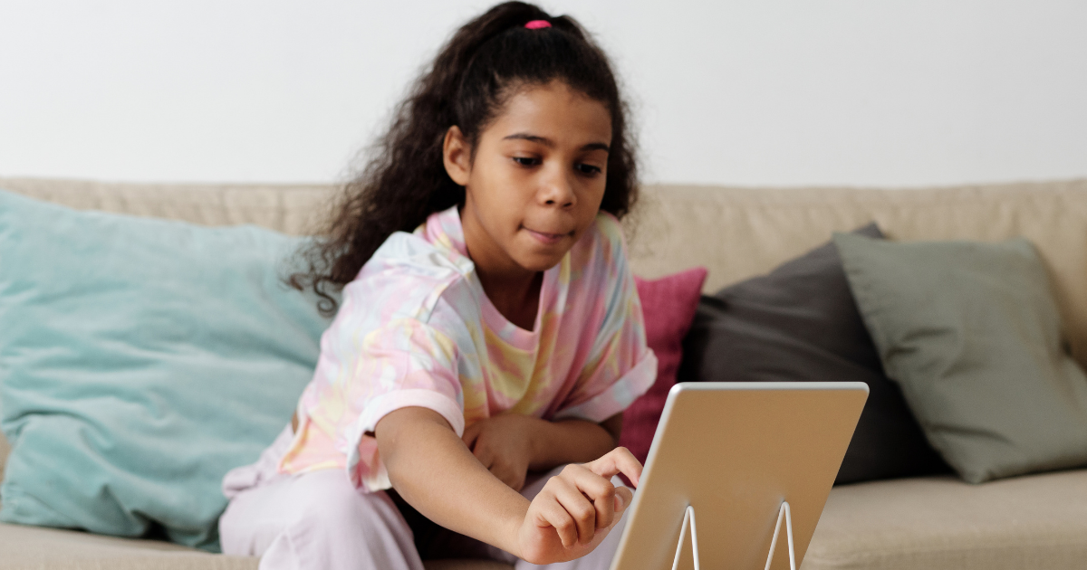 A child reaches over to a tablet propped up on a table