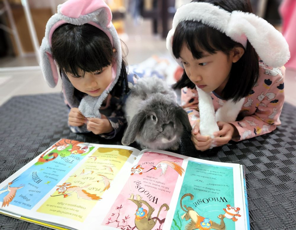 Two children wearing bunny ears read a book to their rabbit