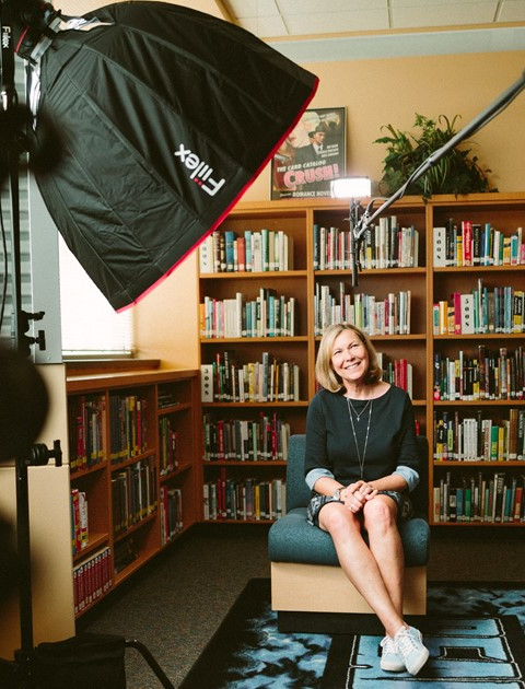 A woman on a filming set with bookshelves in the background.