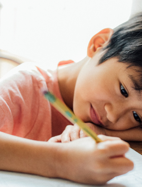 A small child leans over a paper that he is writing on