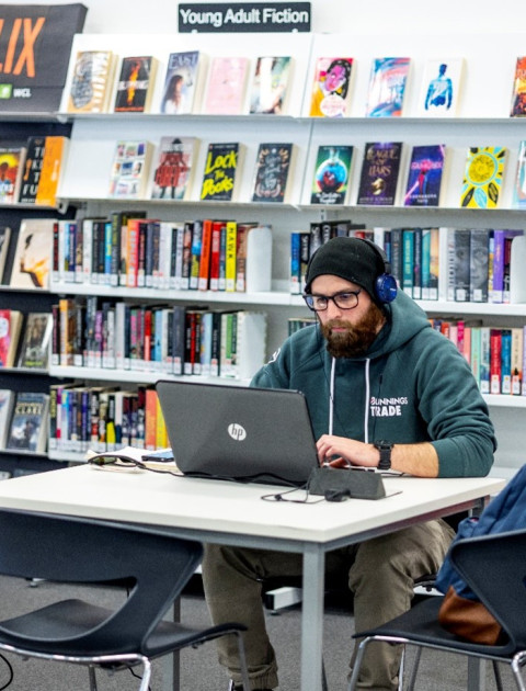 A young person using a laptop in front of the YA fiction shelves