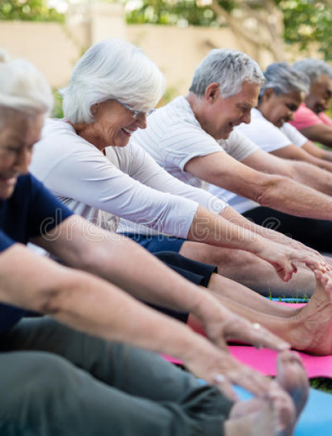 a line of people are sitting with their legs stretched out reaching for their toes