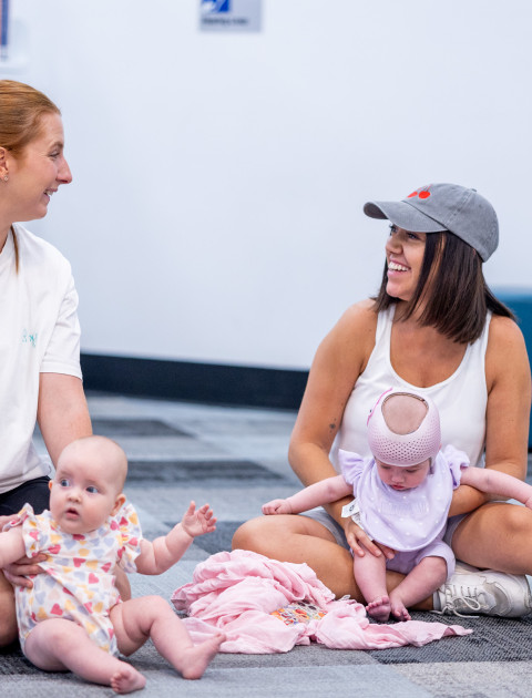 Two mothers and babies sitting in the library and smiling.