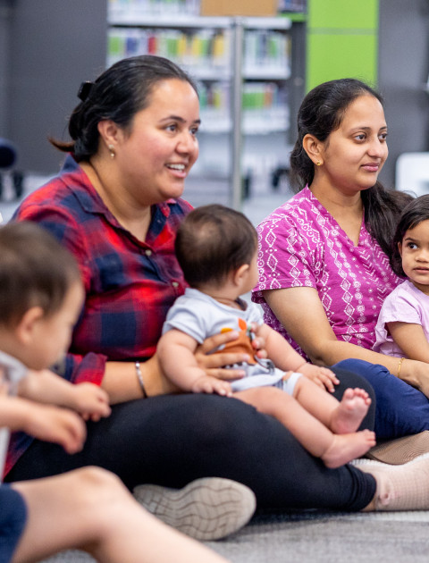 Mothers and children sitting on the floor in the library.