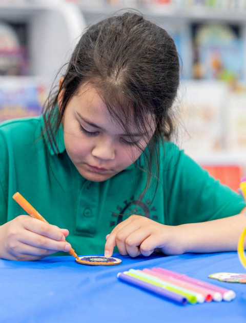 A girl colours in a wooden craft with bright textas.