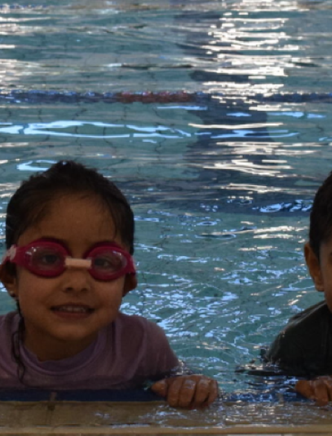 2 adults and 2 kids are in a pool smiling at the camera