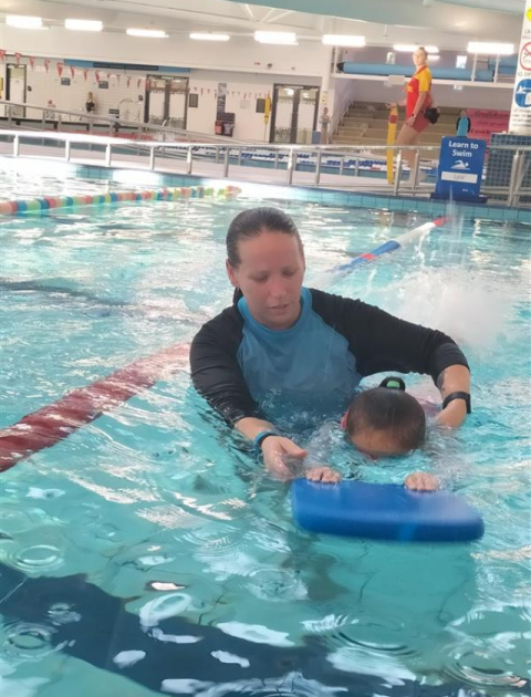 A swimming instructor is helping a child to swim with a float in the pool