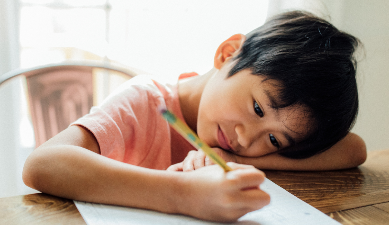 a child leans over a paper with a pencil ready to write