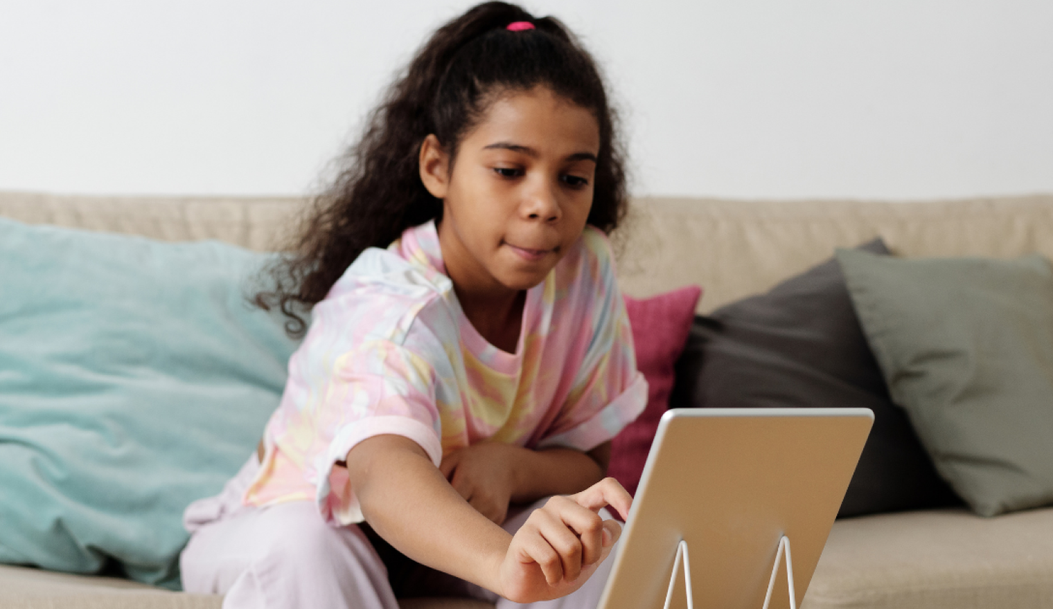 A child reaches over to a tablet propped up on a table