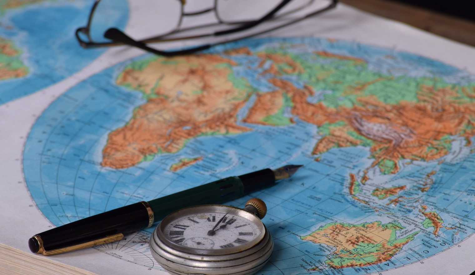 Glasses, a pen, and a pocketwatch on a world map
